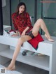 A woman in a red and black dress sitting on a white bench.