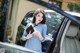 A woman standing next to a car holding a book.