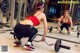 A woman in a red top and black leggings squatting with a barbell.