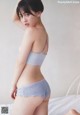 A woman in a gray and pink bra top and panties on a bed.