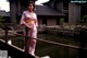 A woman in a pink kimono standing on a wooden bridge.